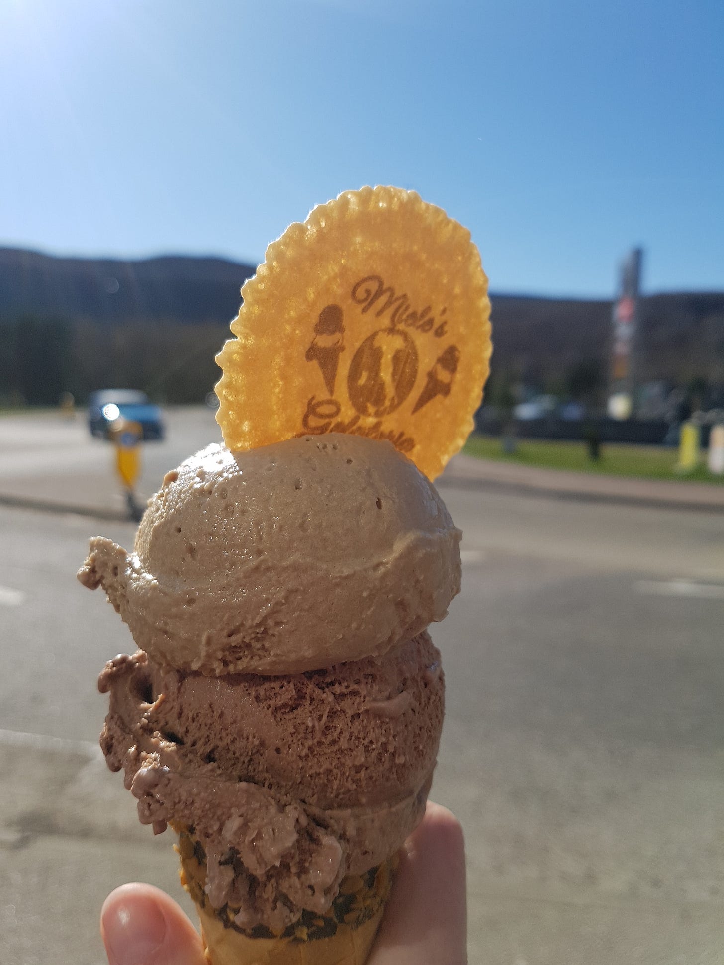 Hand holding up large ice cream cone against a blue sky.