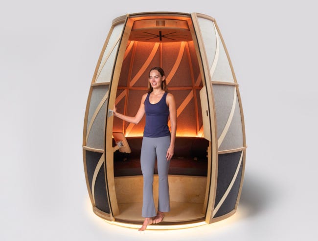 Une jeune femme en tenue de sport sort du pod de méditation, avec un grand sourire