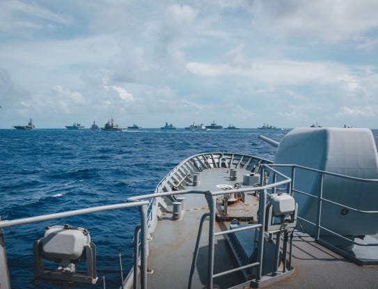 The bow of HMNZS Te Kaha on the sea and its 5-inch gun, with a formation of foreign military vessels in the background. The bow of HMNZS Te Kaha on the sea and its 5-inch gun, with a formation of foreign military vessels in the background.