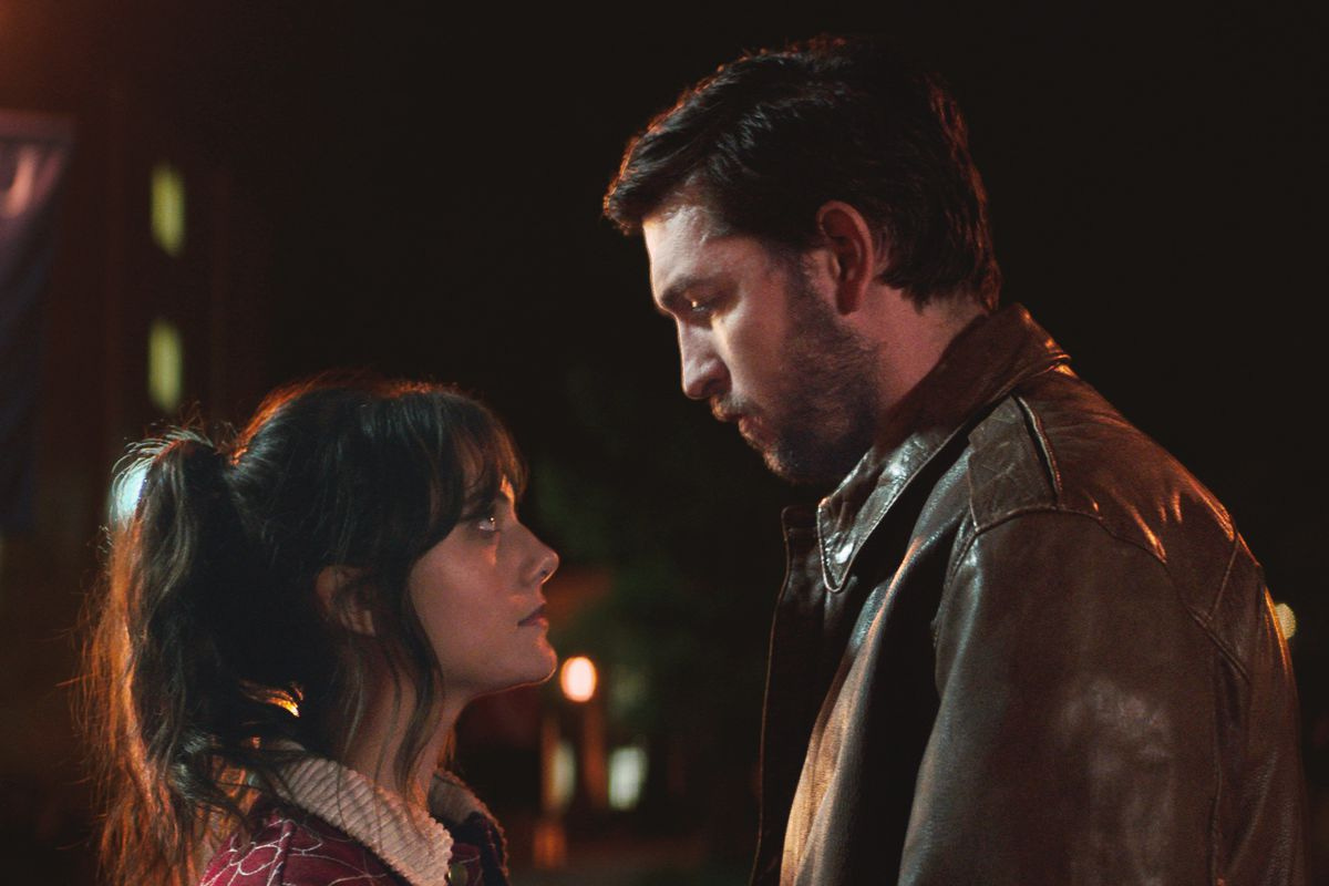 Cat Person actors Nicholas Braun and Emilia Jones gazing into each others eyes under the yellow glow of a streetlight