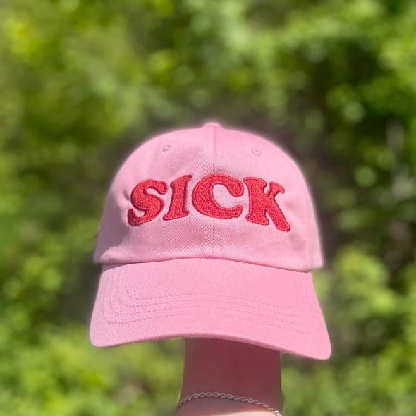 A pink baseball hat with the word SICK in red embroidered letters.