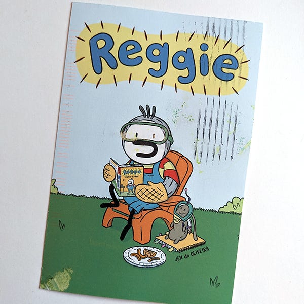 A photo of a postcard of Reggie wearing a snorkel mask and reading a copy of his book while wearing oven mitts and sitting on a lawn chair. 