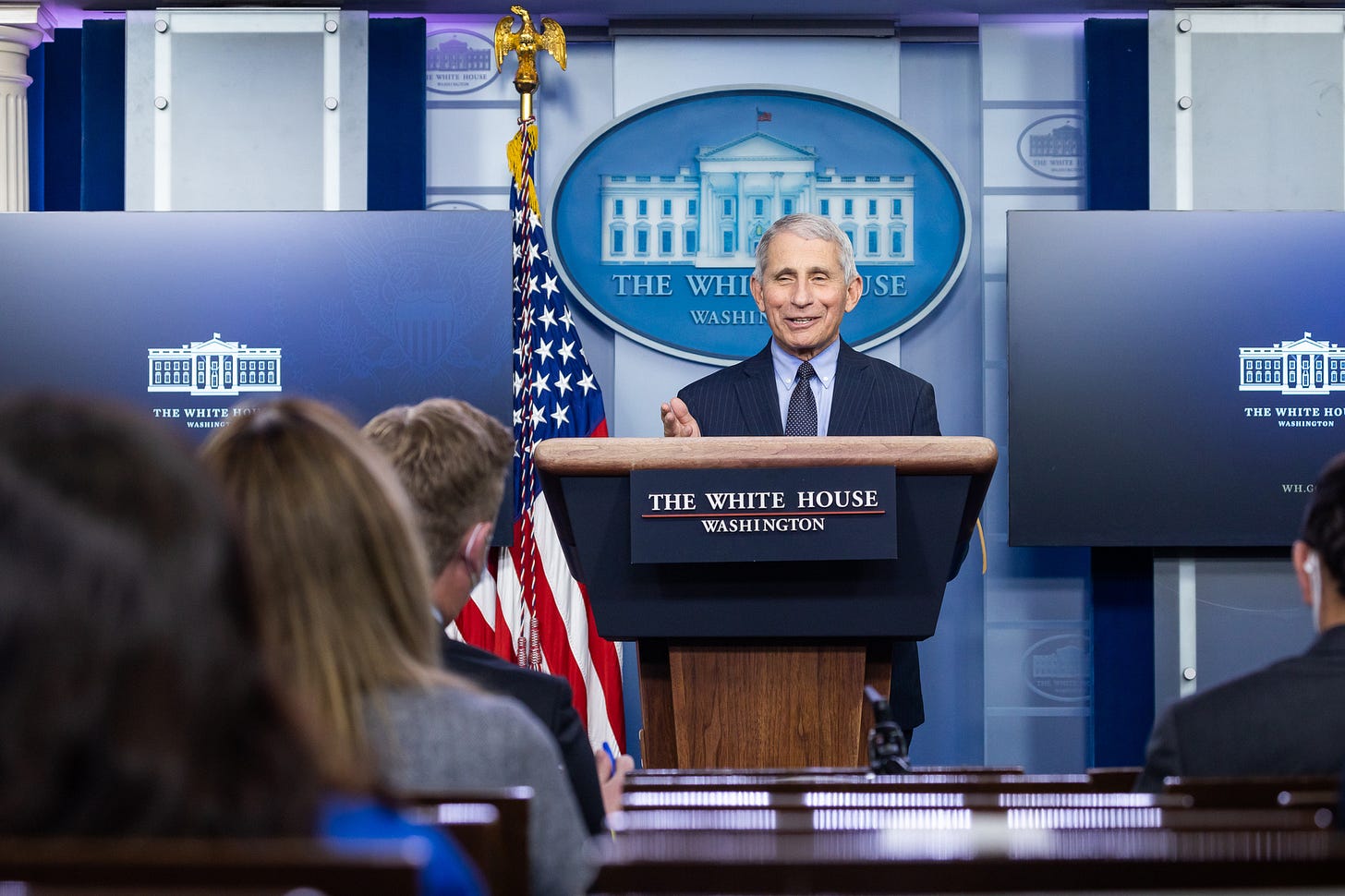 Dr. Anthony Fauci speaks at a podium during a White House press briefing, with the presidential seal behind him.