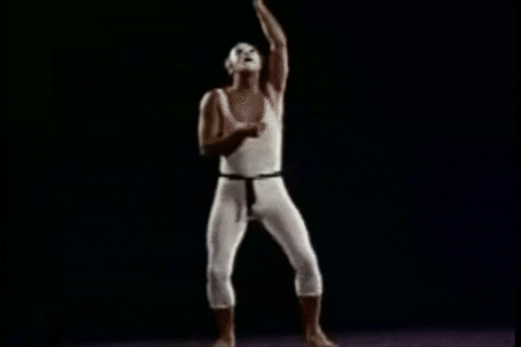 A grainy, vintage archival video of a mime in white clothing standing before a scenic forest backdrop. The mime reaches up and abruptly pulls a heavy, pitch-black shade down over the entire landscape, completely erasing the scenery and ending the frame in a dark, empty void.