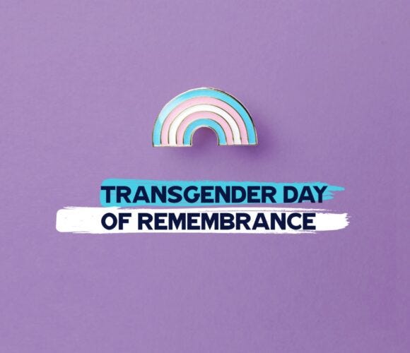 Graphic on a purple background featuring a pastel rainbow in the colors of the transgender pride flag above bold text reading ‘Transgender Day of Remembrance,’ symbolizing honor, visibility, and solidarity for TDoR.