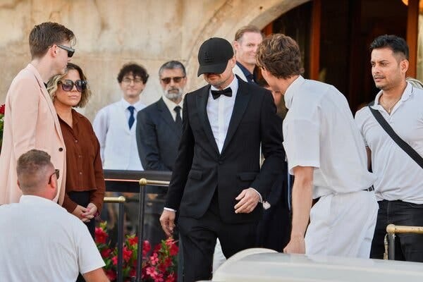 Leonardo DiCaprio, with a black hat largely obscuring his face, walks past several other people.