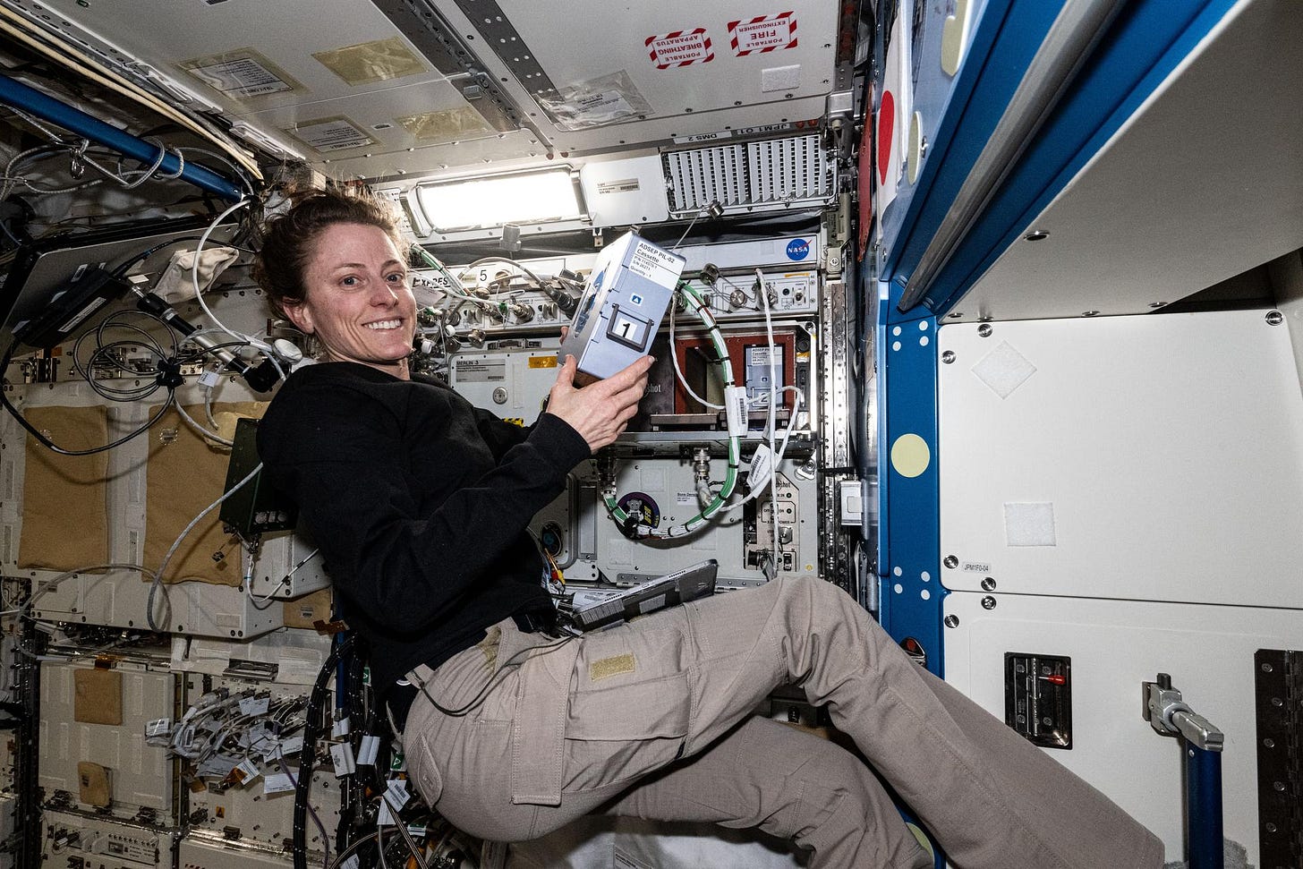 O’Hara, wearing a long-sleeved black shirt and khaki pants, faces the camera and smiles. She is holding a silver rectangular piece of hardware about the size of a box of tissues that has a black handle and a white label on its side. O’Hara, wearing a long-sleeved black shirt and khaki pants, faces the camera and smiles. She is holding a silver rectangular piece of hardware about the size of a box of tissues that has a black handle and a white label on its side.