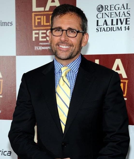 This may contain: a man in a suit and tie standing on a red carpet with his hands together