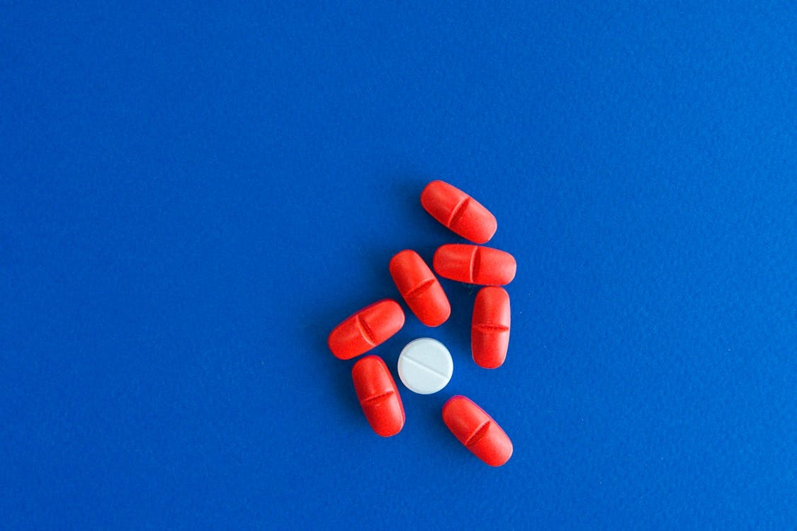 Close-up of red tablets surrounding a single white pill on a blue surface. Stock Photo Close-up of red tablets surrounding a single white pill on a blue surface. Stock Photo