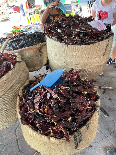 A nine image gallery showing dried chiles, coffee, cocoa beans, and sugar for sale at the market.