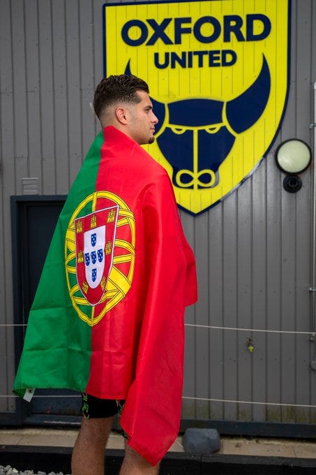 Rúben Rodrigues poses outside the Oxford United Training Ground with a Portuguese flag.