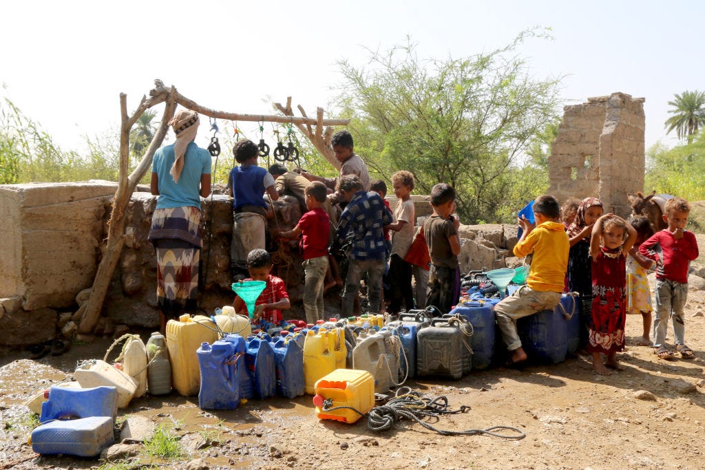 a group of brown children gather around a water well and cannisters of water a group of brown children gather around a water well and cannisters of water