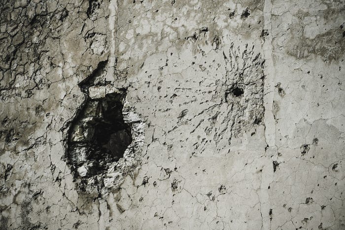 A crumbling concrete wall. It shows evidence of damage by gunfire and erosion. A crumbling concrete wall. It shows evidence of damage by gunfire and erosion.