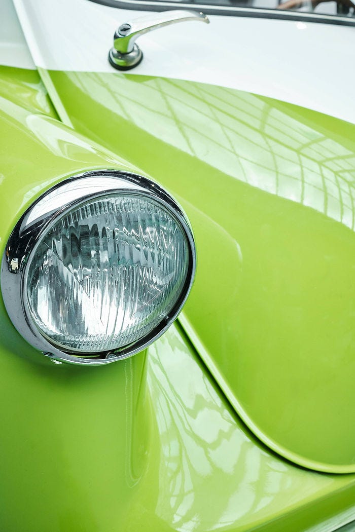 Close-up of a lime green and white classic car's headlight, reflecting light in an indoor setting with curved lines and glossy finish.