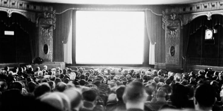 This may contain: an auditorium full of people sitting and standing in front of a large window