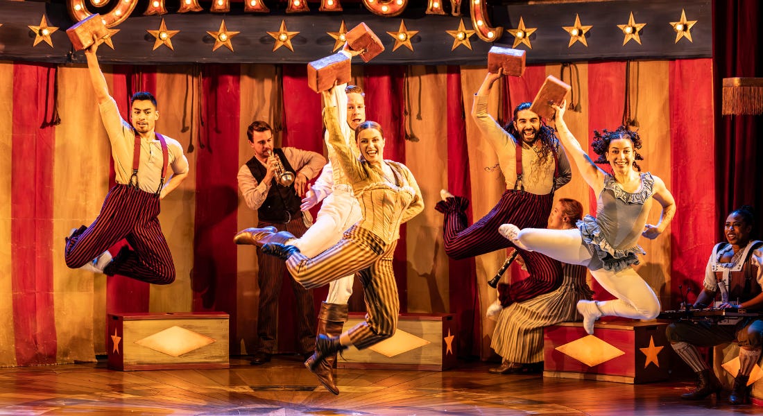 Five performers jumping in the air on the stage, holding bricks, with a red and white backdrop behind them Five performers jumping in the air on the stage, holding bricks, with a red and white backdrop behind them