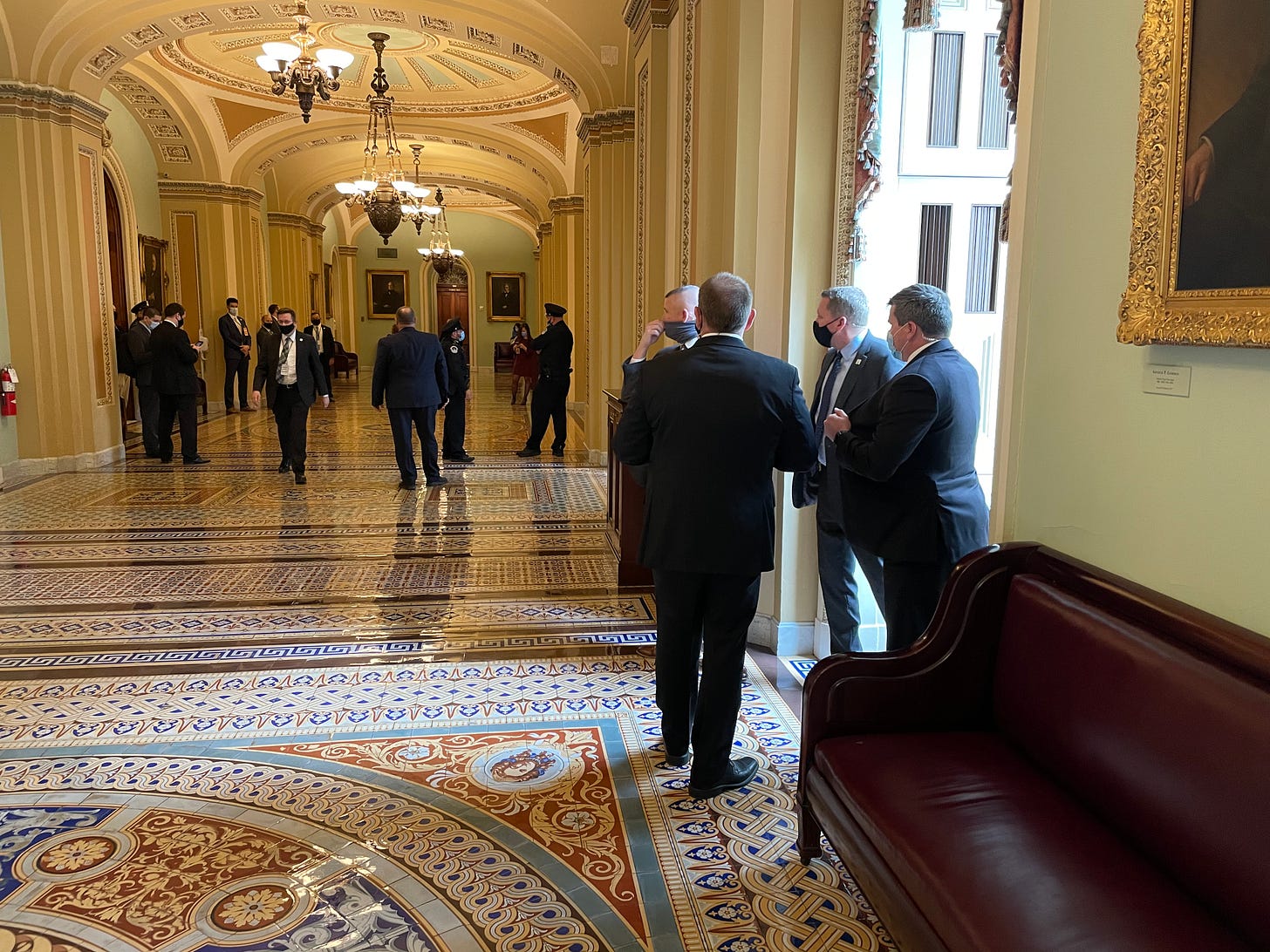Four officers in suits near a window look back towards a larger group of officers near an entrance to US Senate floor on Jan. 6, 2021 Four officers in suits near a window look back towards a larger group of officers near an entrance to US Senate floor on Jan. 6, 2021