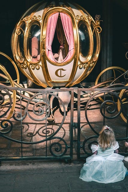 A display exhibit of Cinderella's carriage with a young blonde girl sitting on the ground to the right of the carriage, looking up at it.