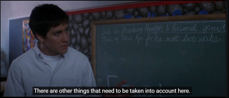 Movie still from the movie Donnie Darko where the protagonist stands near a school chalkboard. 