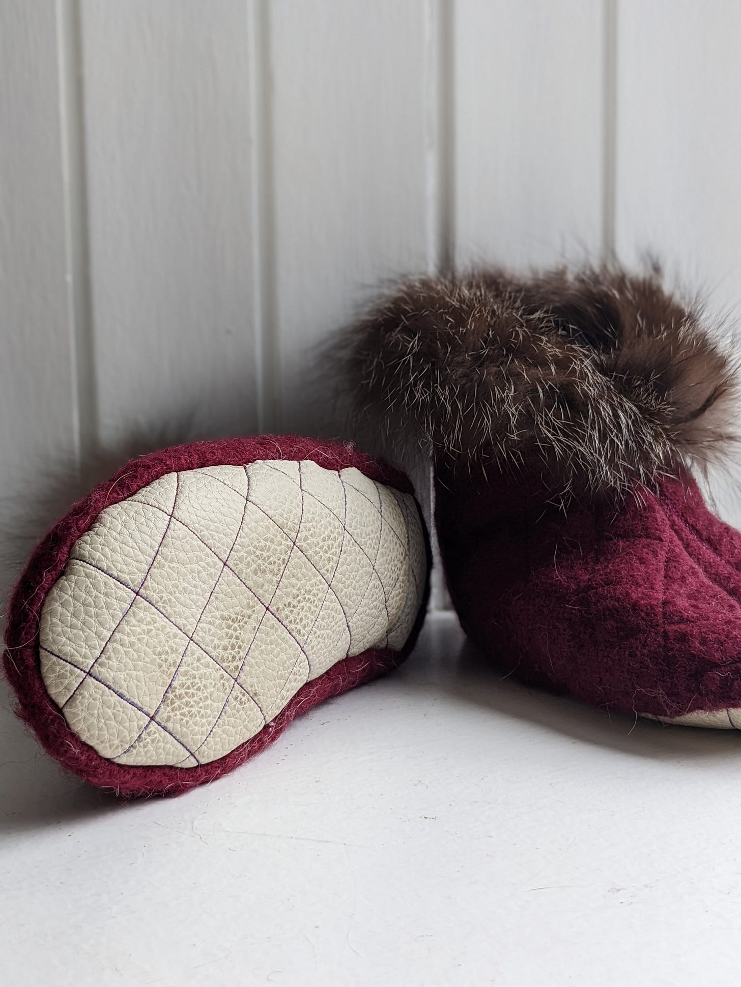 A pair of burgundy wool slippers, with one lying sideways to show the white leather sole