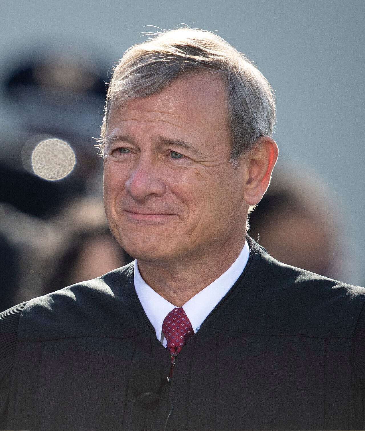 John Roberts head and shoulder shot in 2021; smiling smugly, gray hair, red tie under robe John Roberts head and shoulder shot in 2021; smiling smugly, gray hair, red tie under robe