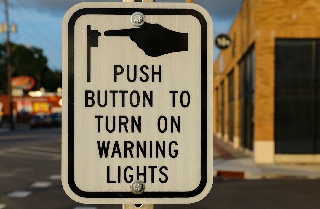 a hand pointing at a sign that says push button to turn on warning lights