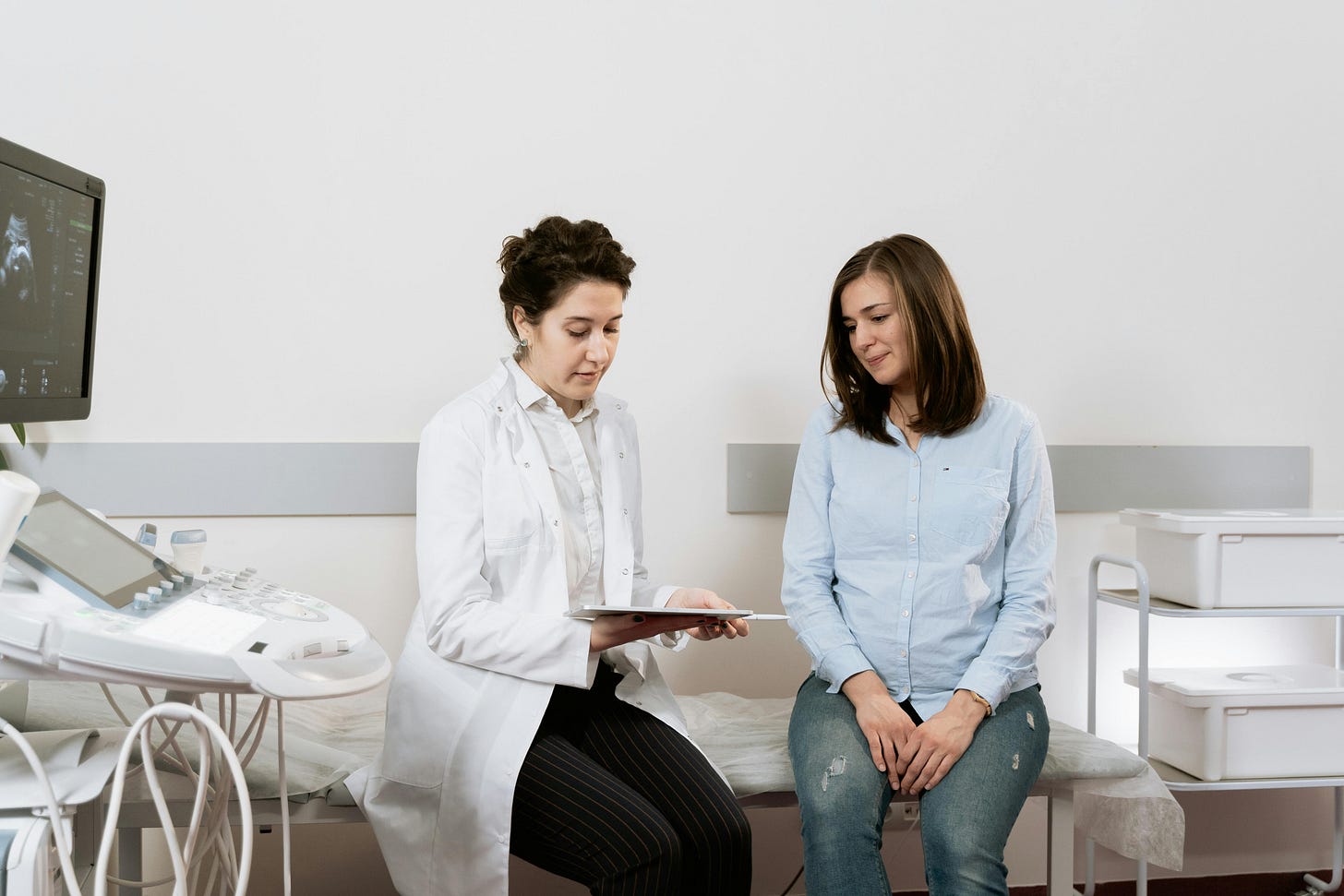 Photograph of a doctor with a chart talking to a pregnant woman in a doctor's office