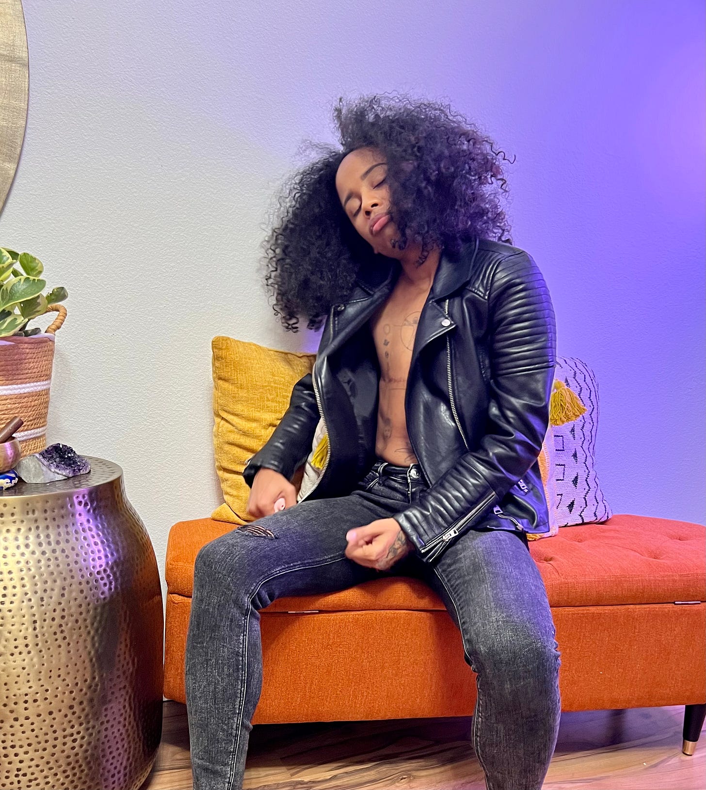 Raw sitting on an orange couch wearing a black leather jacket and distressed jeans.