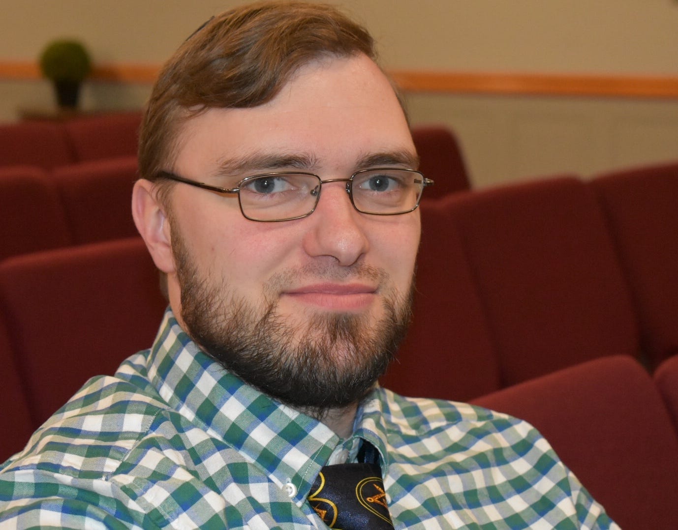May be an image of 1 person, beard, sitting, eyeglasses and indoor