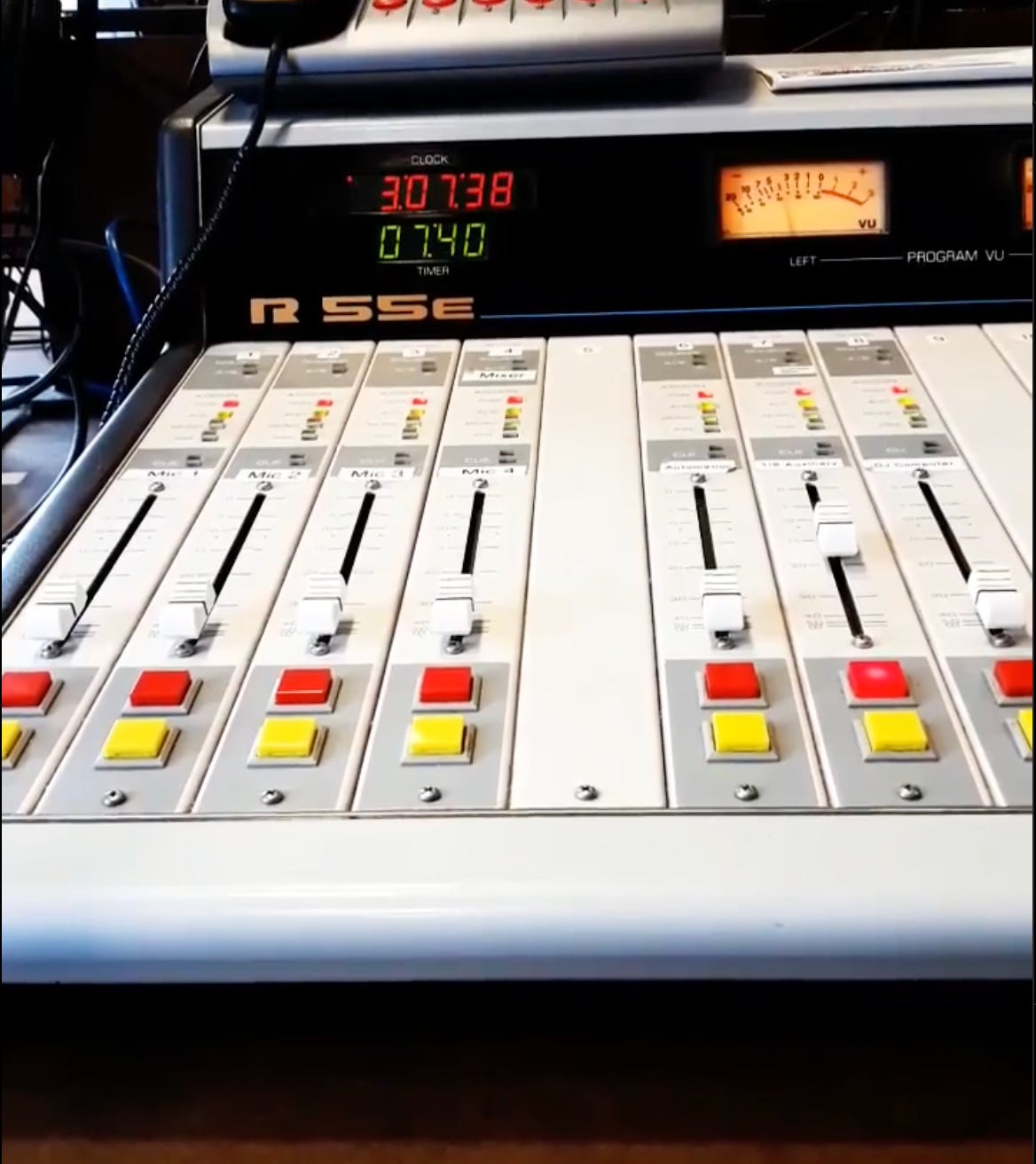 Image of a sound board, red and yellow buttons below silver faders, a digital display of time, and the tangled cord of a phone resting on top of the console. Image of a sound board, red and yellow buttons below silver faders, a digital display of time, and the tangled cord of a phone resting on top of the console.
