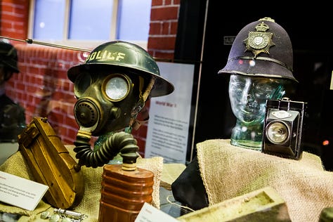 Photographs showing tin hats with 'Police' written on them, bullseye lamps, a hand bell, metal County Police signs and medals.