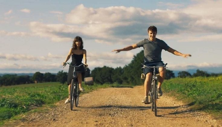 This may contain: two people riding bikes down a dirt road