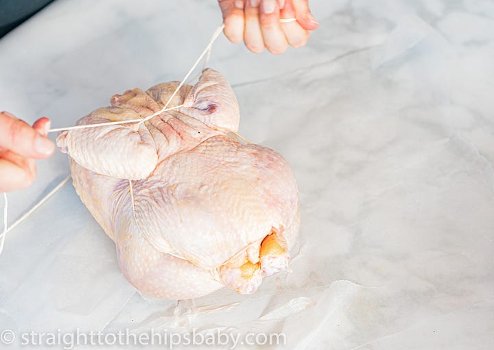 Hands trussing a whole raw chicken with butcher's twine before roasting