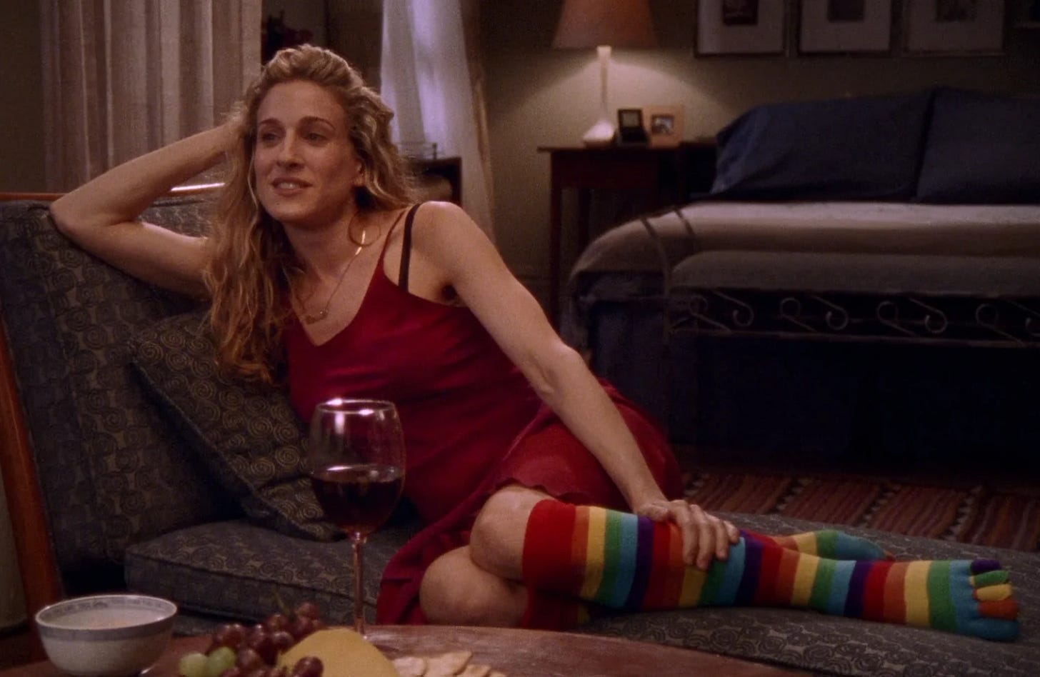 Carrie wears a red slip and rainbow toe socks while lounging on the couch.
