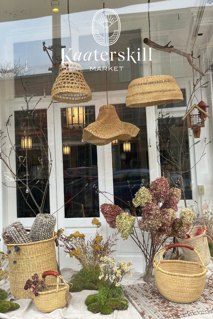 This contains: Kaaterskill Market in Catskill, New York spring  shop window display with baskets, woven lighting, rugs and dried flowers.