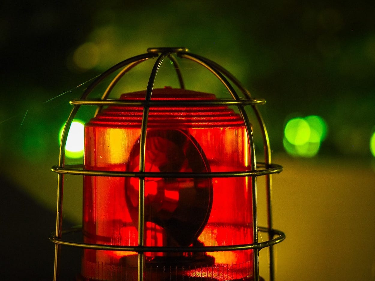 Image shows a red emergency light in a gold-colored wire cage on top of an emergency vehicle. Image shows a red emergency light in a gold-colored wire cage on top of an emergency vehicle.