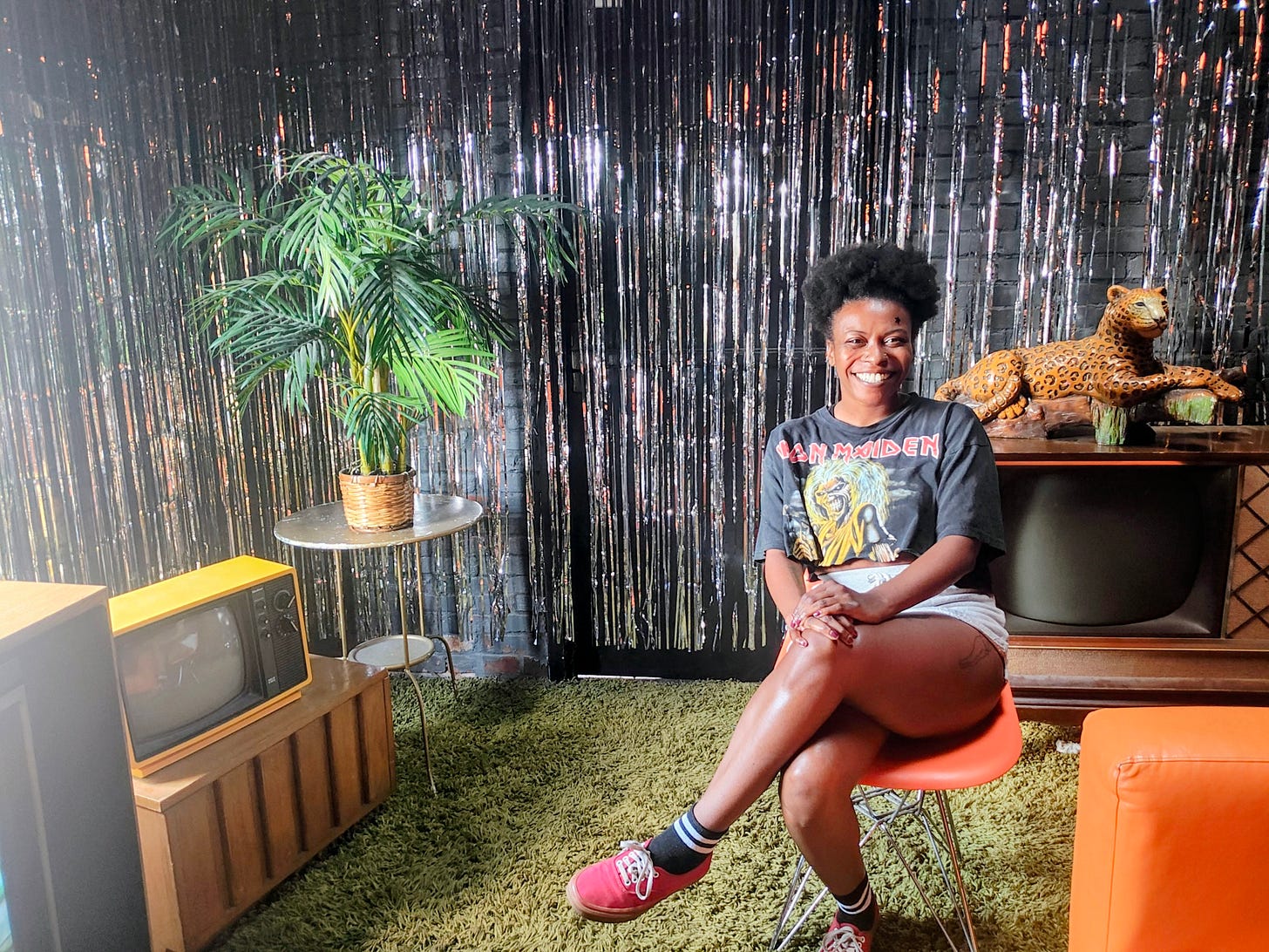 smiling black woman wearing t shirt sitting in room with silver strands hanging around her