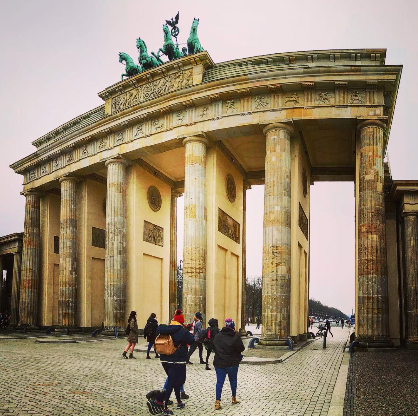Brandenburg Gate in Berlin, with its tall neoclassical columns and the Quadriga statue on top, as people walk beneath the archway on a cold day.