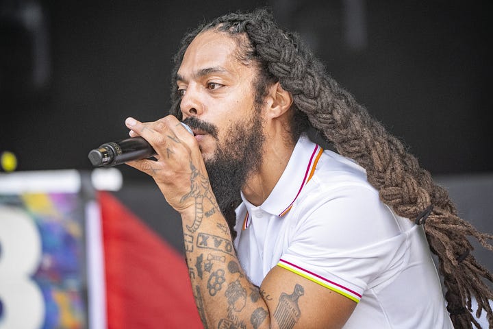 1. Long haired blond Christian performer Sean Feucht with his guitar in concert. 2. Long-dreadlocked, bearded and tattooed punk-rap performer Pascal Robinson-Foster of Bob Vylan, on the mic in concert.
