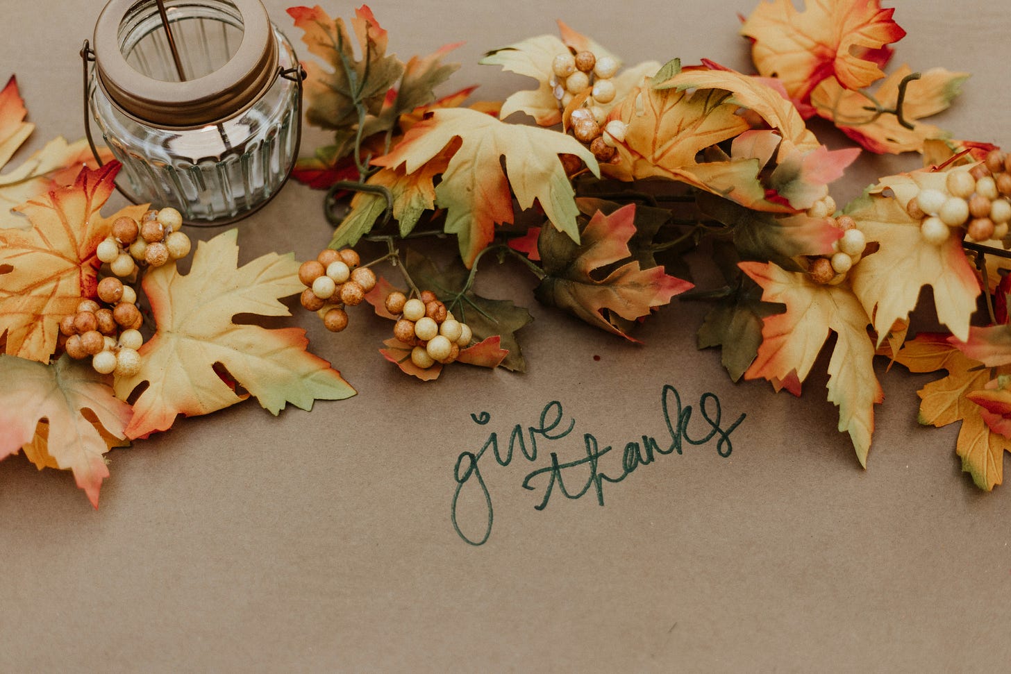 Autumn leaf garland and mason jar candle on a table with "give thanks" written Autumn leaf garland and mason jar candle on a table with "give thanks" written