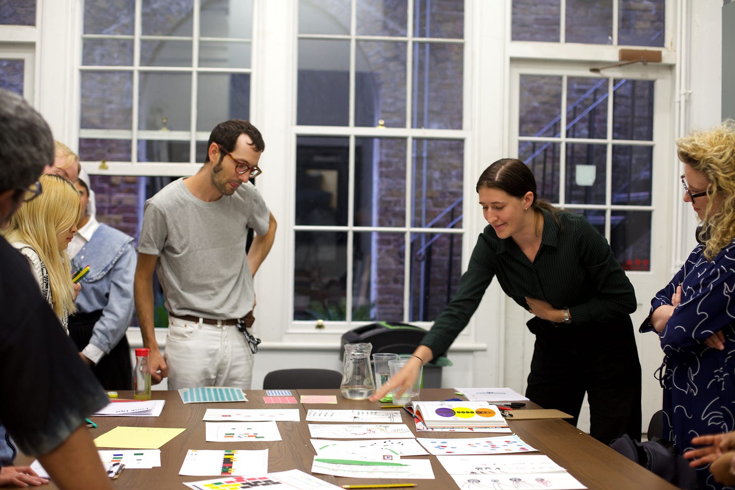 A data visualisation workshop in the vaults at Makerversity, Somerset House. A group of participants huddle around a table, looking at hand-drawn data visualisations.