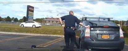 A police officer touches the back of a car after pulling it over on the highway.