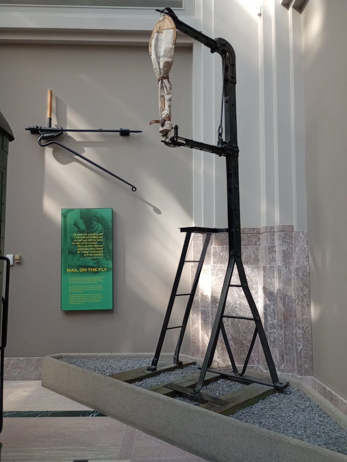 Photo of man in early 20th century sorting mail on train, mailbags and slots on mail train carriage in museum. Mail catcher used by moving train