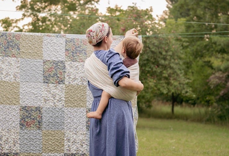 a woman holding a baby next to a quilt