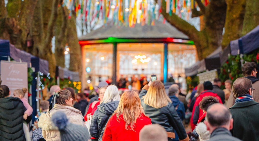 A crowd of people walking to a market with stalls either side, with a gazebo at the front