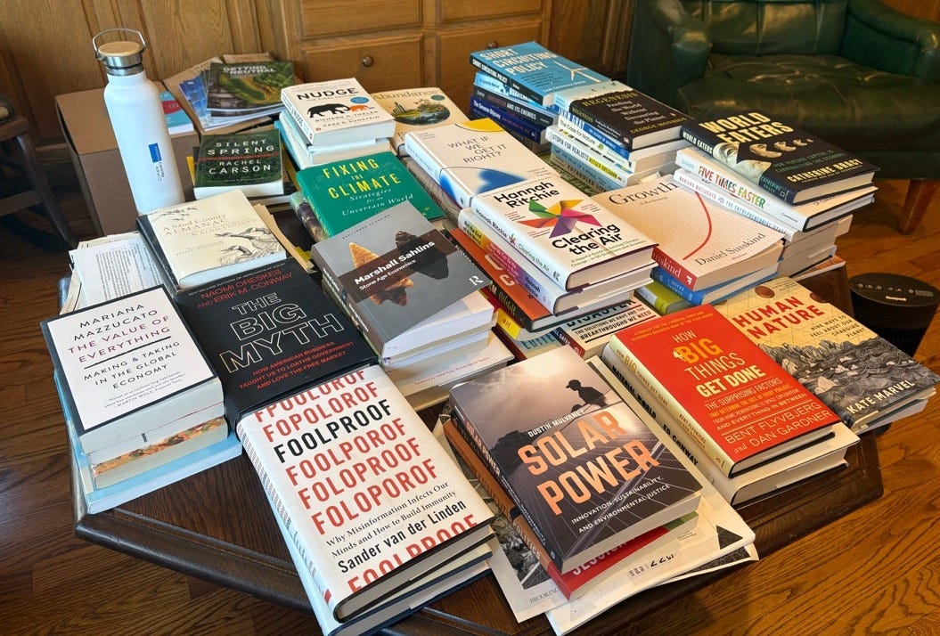 A number of stacks of books on a table. The books all deal with climate change, economics, and social issues. A number of stacks of books on a table. The books all deal with climate change, economics, and social issues.