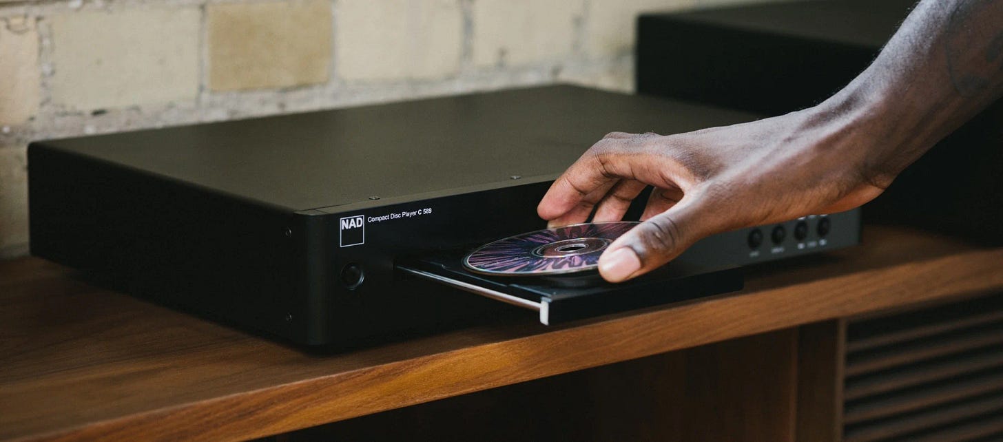 A hand dropping a CD into the tray of an NAD C 589 CD player.