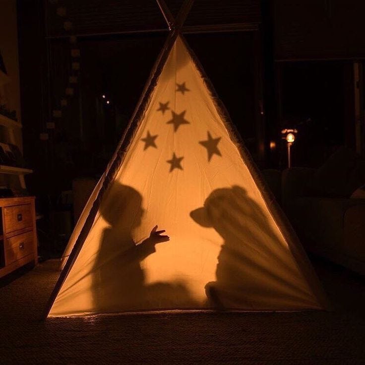 This may contain: the shadow of a person standing in front of a lit up teepeet with stars on it
