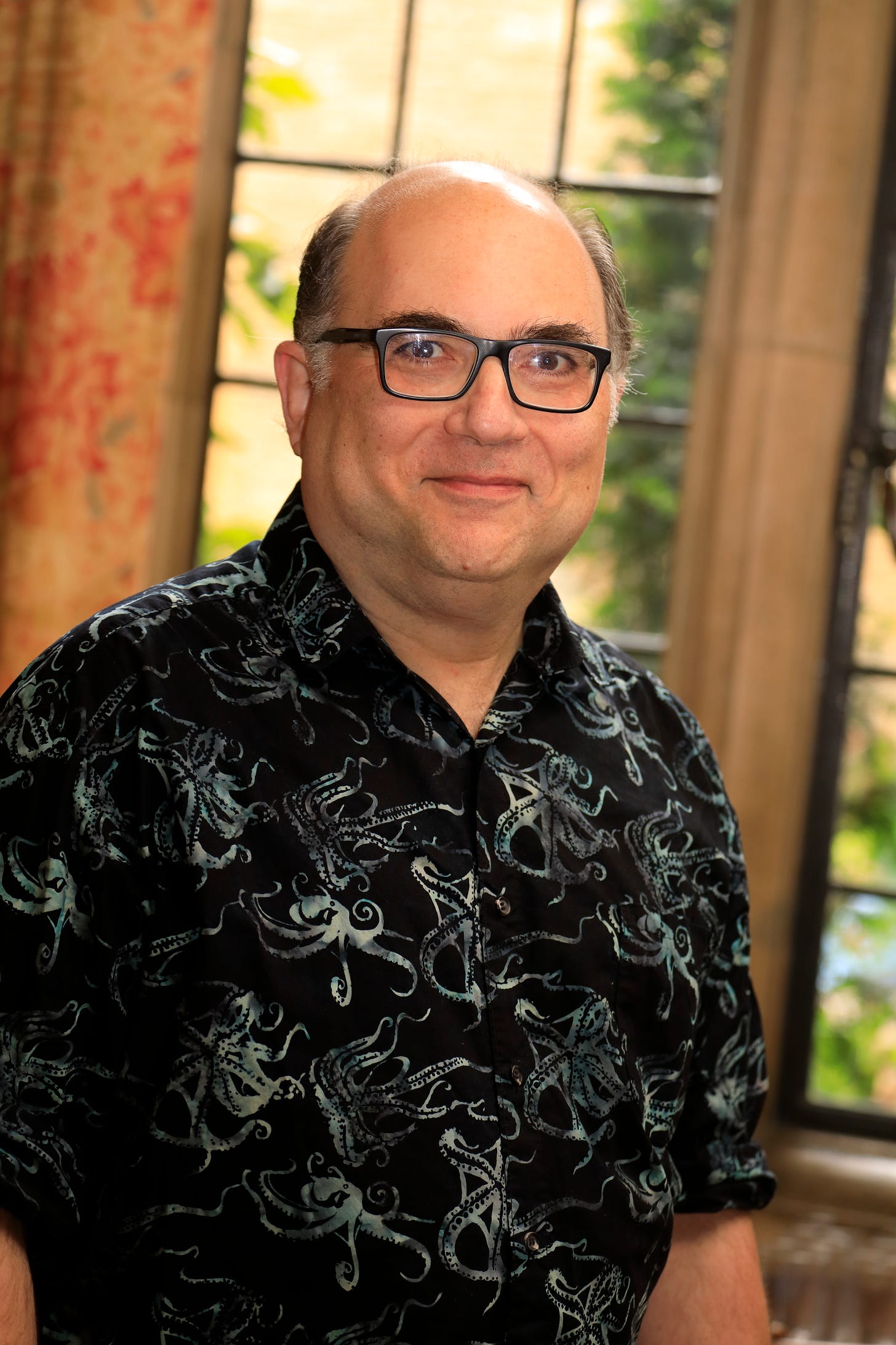 A strikingly handsome man-- Okay, I guess I should be more honest: An aging, bespectacled bald guy, wearing a really cool shirt with an octopus design on it, smiles at the camera. In the background is a window, with the morning sun shining through. A strikingly handsome man-- Okay, I guess I should be more honest: An aging, bespectacled bald guy, wearing a really cool shirt with an octopus design on it, smiles at the camera. In the background is a window, with the morning sun shining through.
