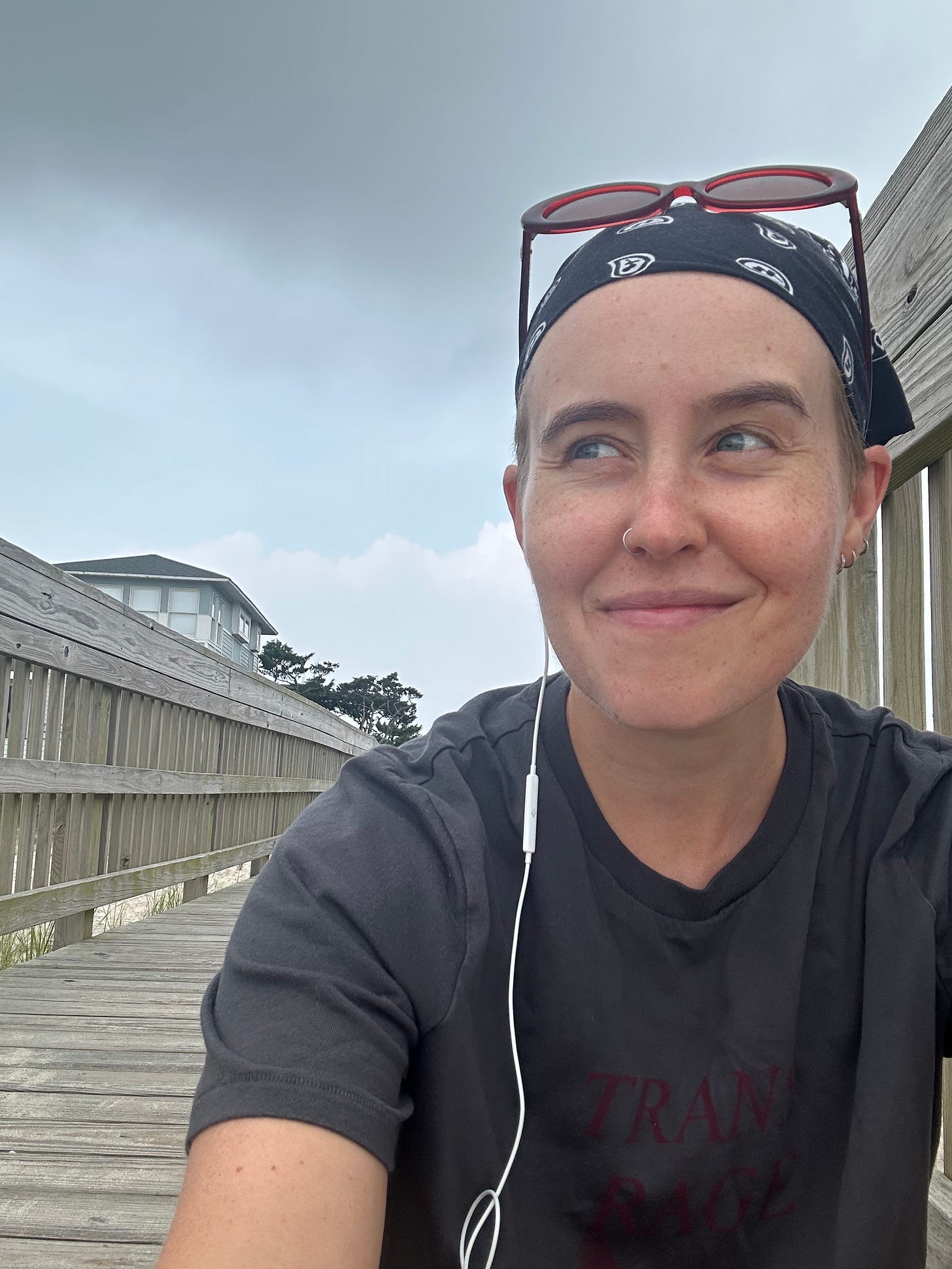 Fi sits on the beach stairs in a bandana and t shirt with dark clouds and lighter clouds behind them